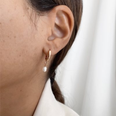 עגיל חישוק מצופה זהב עם תליון פנינה טבעית קטנה, על אוזן של אישה עם שיער חום אסוף חלקית. ניתן גם בכסף אמיתי 925 ורוז גולד