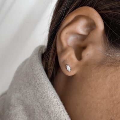 עגיל ג'ורדי כסף אמיתי 925 בצורת אבן מרקיזה משובצת זירקוניה מבריקה, על תנוך האוזן עם שיער אסוף ומעיל בצבע בז' רך.