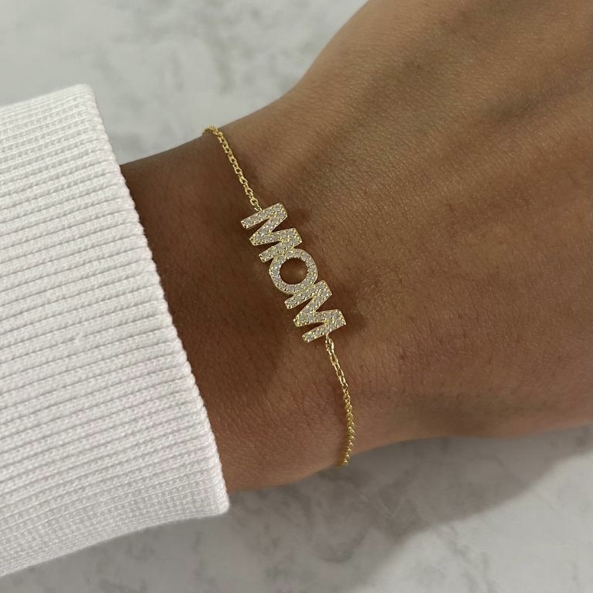 צמיד כסף 925 בציפוי זהב עם תליון אותיות MOM משובצות זרקונים על יד של דוגמנית
