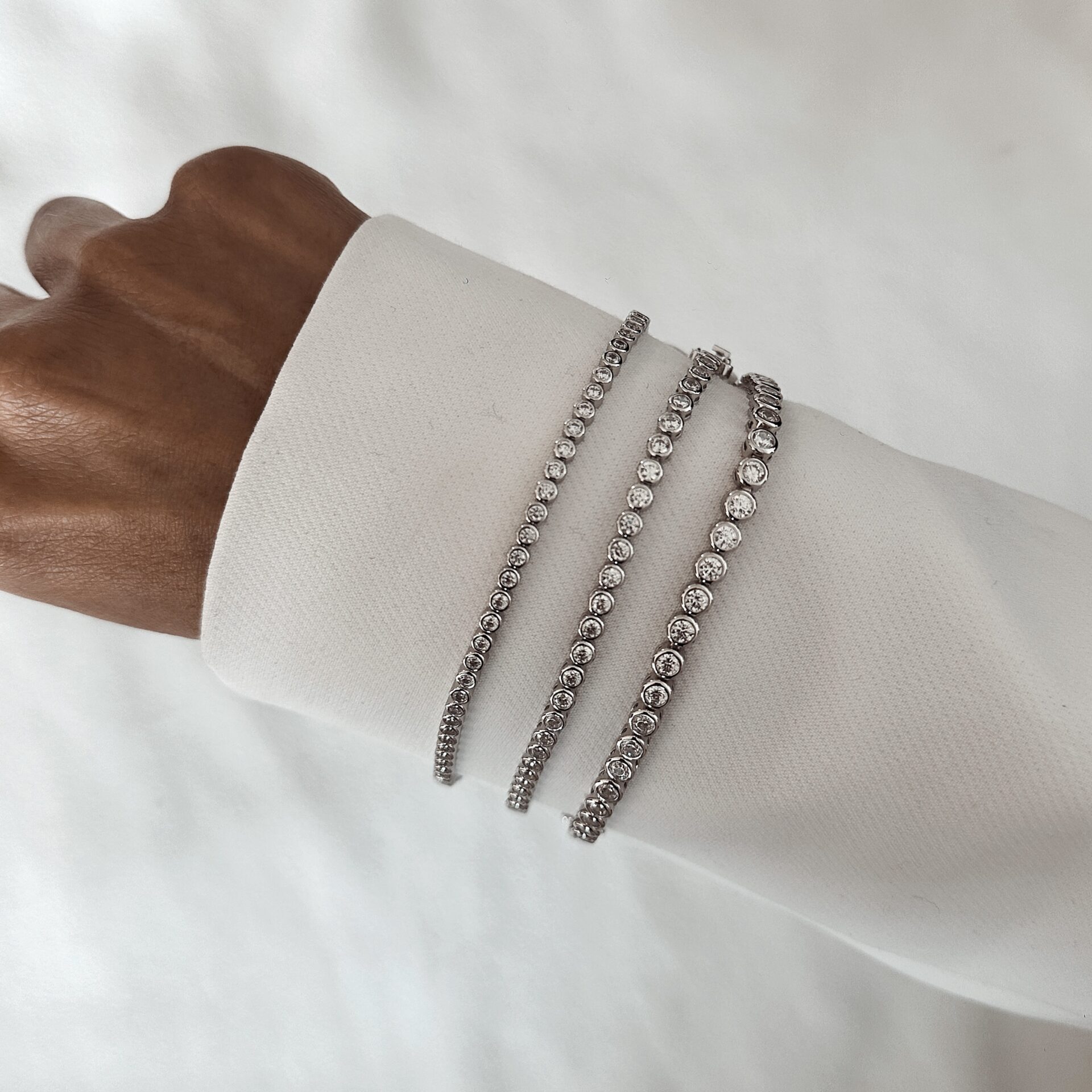 צמיד טניס עיגולים כסף אמיתי 925 משובץ זרקונים בצורת עיגול לאורך כל הצמיד לנשים שלושה צמידי טניס כסף 925 משובצים זרקונים על יד של דוגמנית לבושה בחולצה לבנה