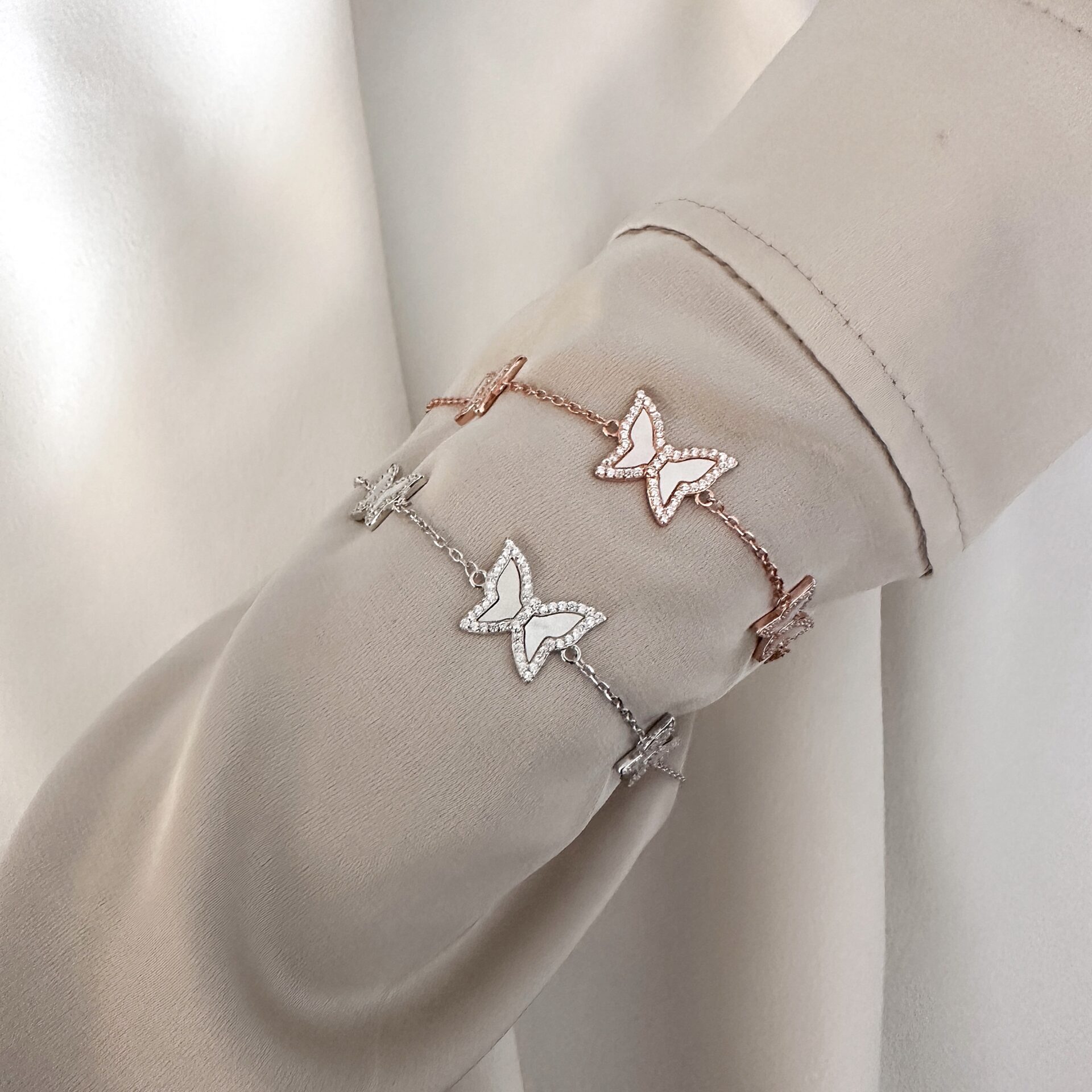 צמיד פרפרים כסף 925 בציפוי רוז גולד וציפוי כסף עם תליון פרפר משובץ זרקונים על יד של דוגמנית לבושה בבד בצבע חאקי