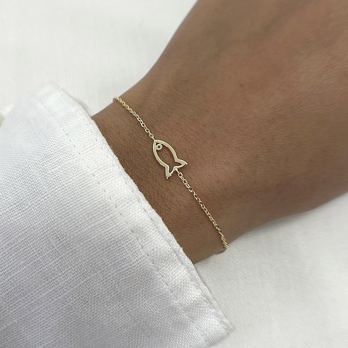 צמיד כסף 925 בציפוי זהב עם תליון דג עדין על יד של דוגמנית לבושה בחולצה לבנה