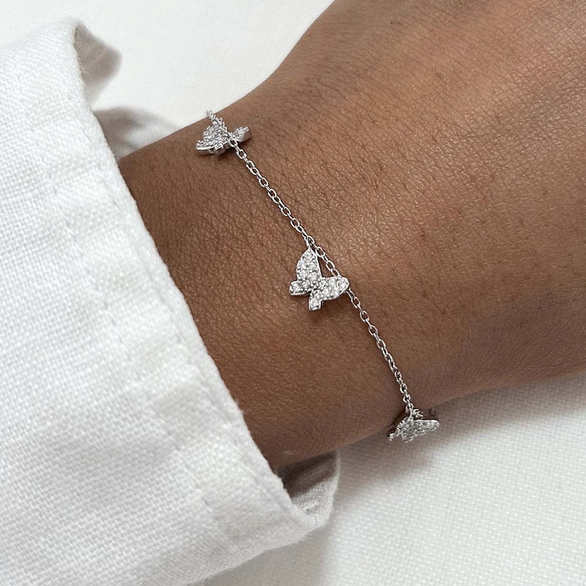 צמיד כסף 925 עם תליון פרפרים משובצי זרקונים על יד של דוגמנית לבושה בחולצה לבנה