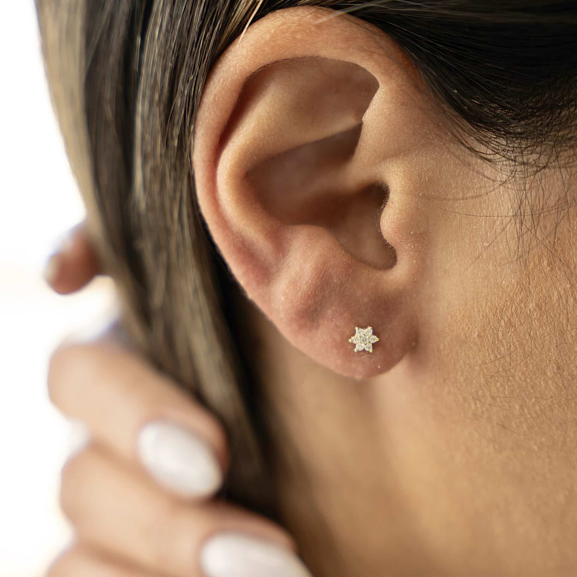 עגיל כוכב כסף אמיתי 925 בציפוי זהב על אוזן של דוגמנית צמוד עם ציפורניים ולק ציפורניים מטופחות