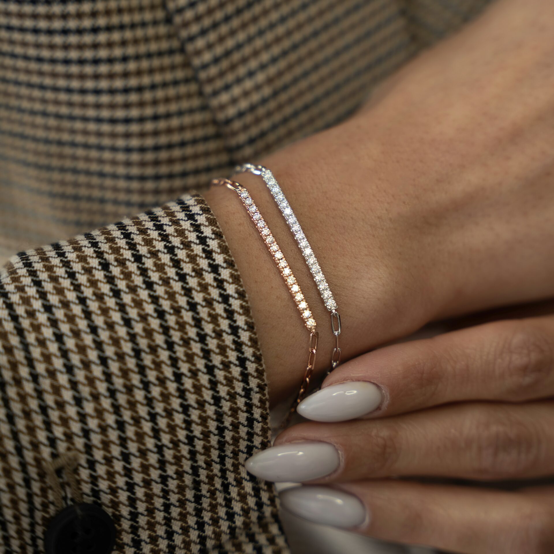 צמיד ארטמיס כסף אמיתי 925 ורוז גולד משובצים זרקונים נוצצים על פרק יד של אישה עם ציפורניים לבנות ומעיל משבצות