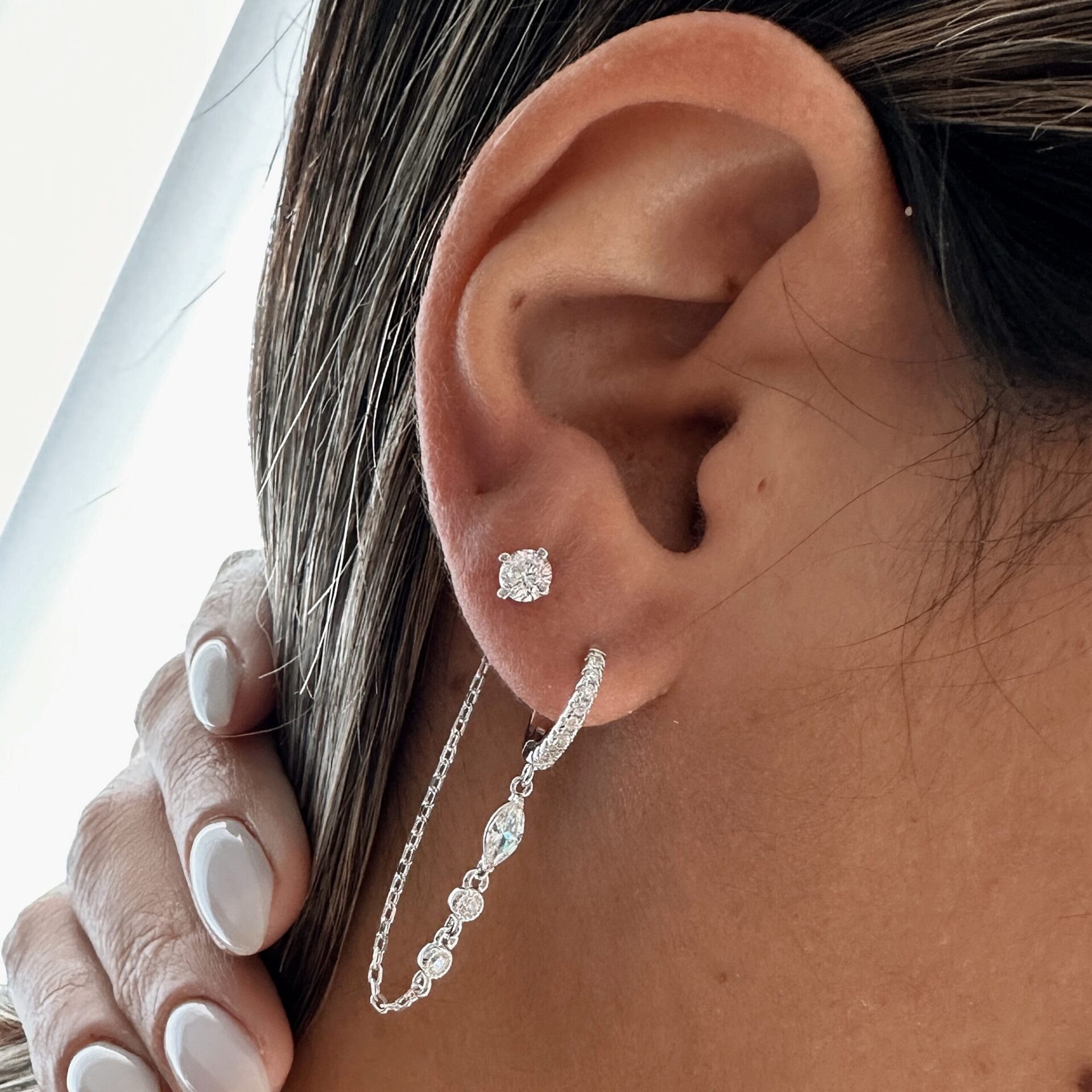 עגיל ויקטוריה חישוק כסף אמיתי סטרלינג 925 עם שרשרת משובצת זירקונים נוצצים המחוברת לעגיל נוסף לחור שני שכולו זרקון על האוזן של דוגמנית עם לק על ציפורניים.