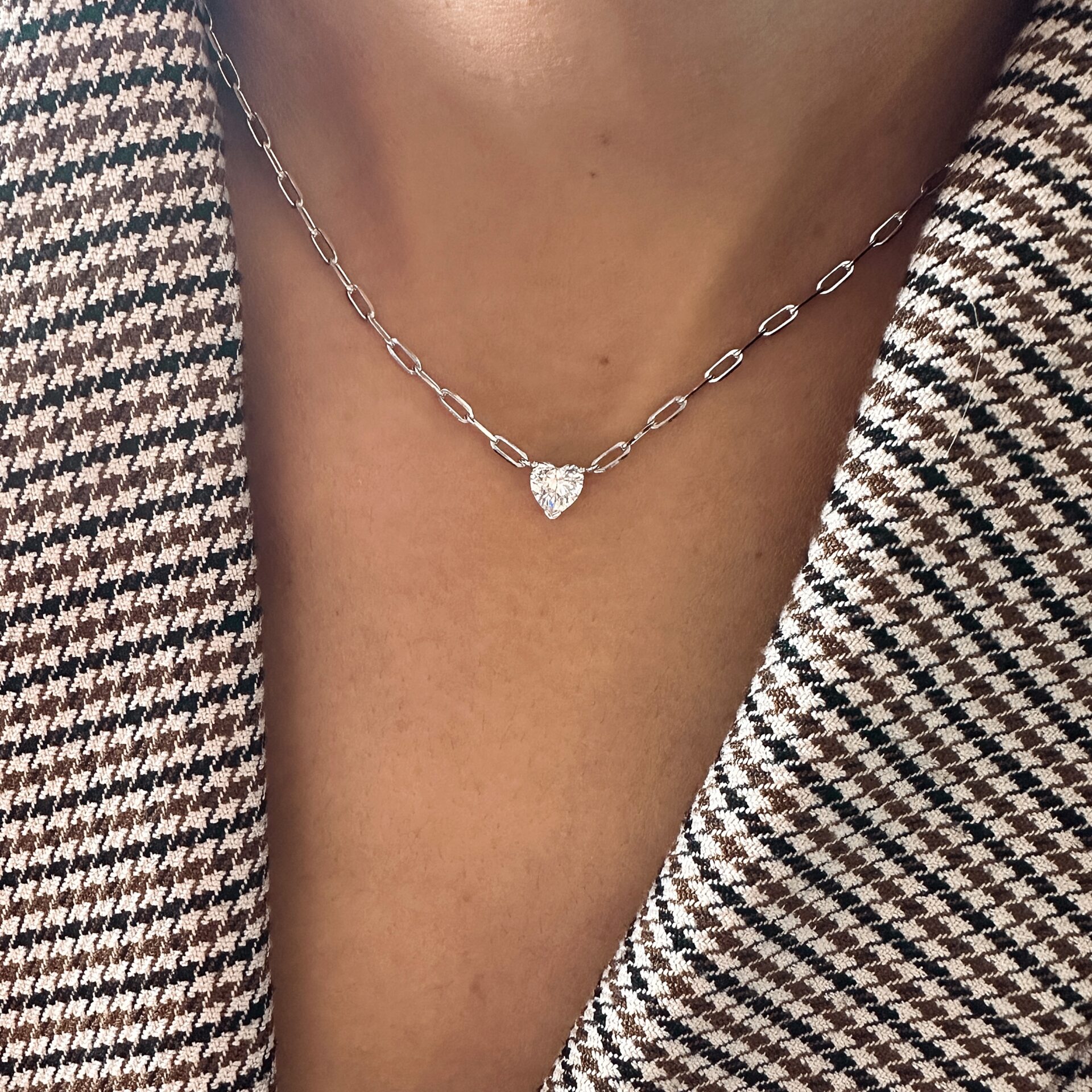 שרשרת כסף אמיתי 925 עם חוליות שטוחות ועיצוב מודרני, מעוטרת בתליון יהלום או זירקוניה נוצצת בצורת לב. מוצגת על צוואר אישה הלובשת ז’קט טוויד קלאסי.