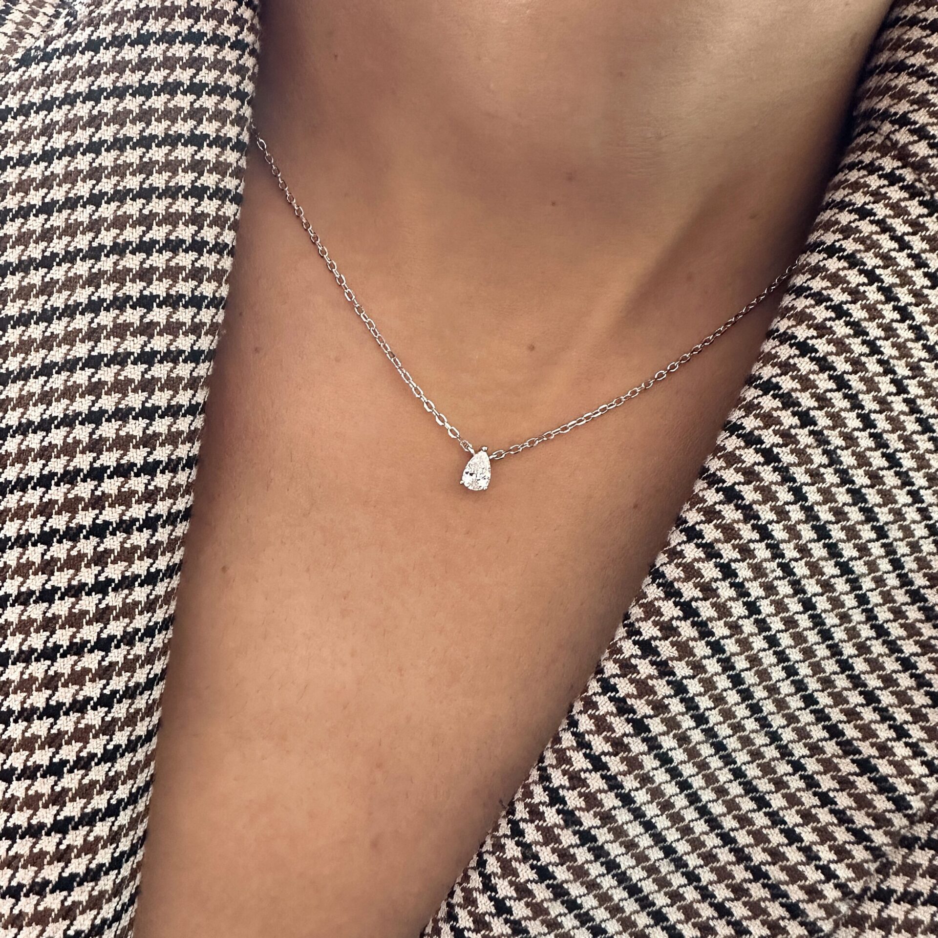 שרשרת טיפה סאני כסף אמיתי 925 עדינה עם תליון יהלום בצורה טיפה, ענודה על צוואר אישה הלובשת ז’קט טוויד בדוגמת פייד דמקה בגווני חום ולבן