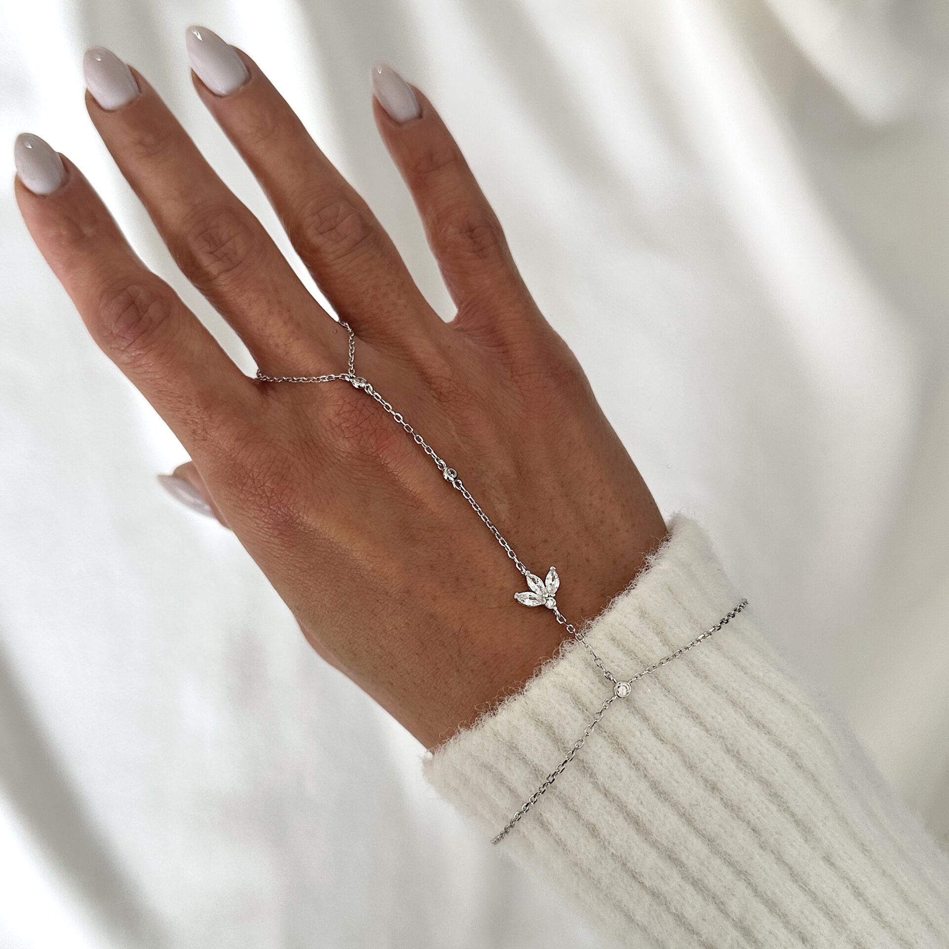 צמיד טבעת כסף 925 עם תליון עלה משובץ זרקונים על יד של דוגמנית לבושה בסוודר לבן