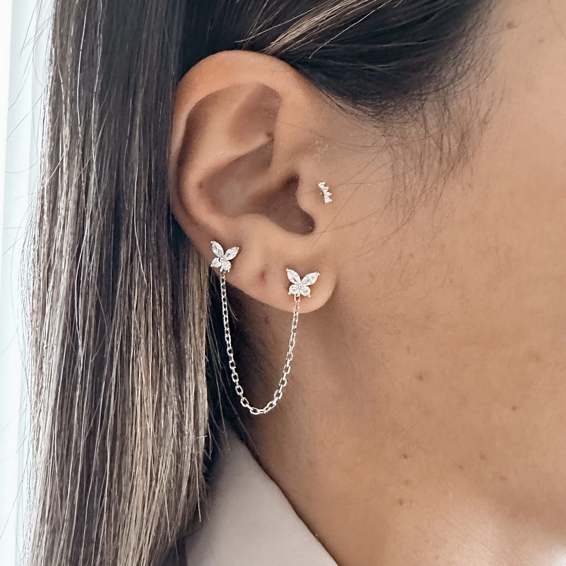 עגילי פרפר כפולים מכסף משובצי זרקונים, מחוברים בשרשרת עדינה, על אוזן בנוסף עגיל הליקס קטן על אישה דוגמנית עם שיער מטופח
