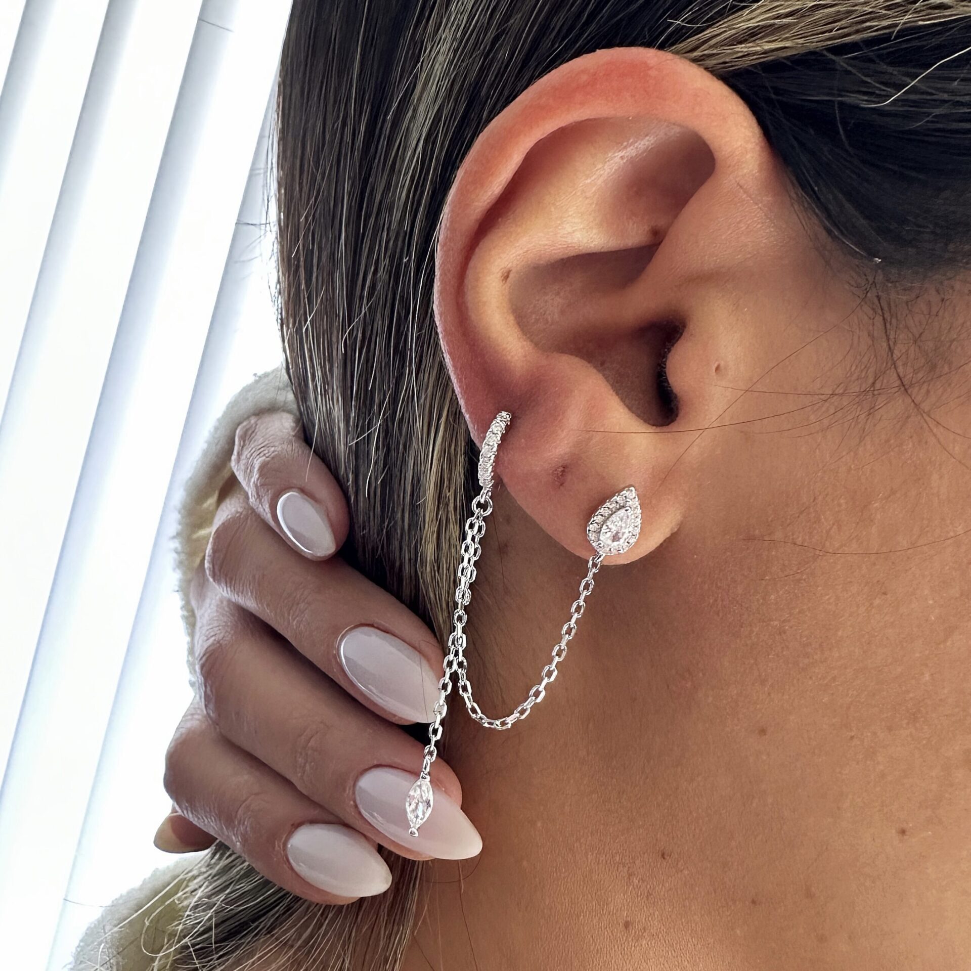 עגיל טיפה כפול על אוזן של דוגמנית מחובר עם שרשרת לעגיל חישוק עם שרשרת שיורדת ותליון בסוף כסף אמיתי 925 משובץ זרקונים.