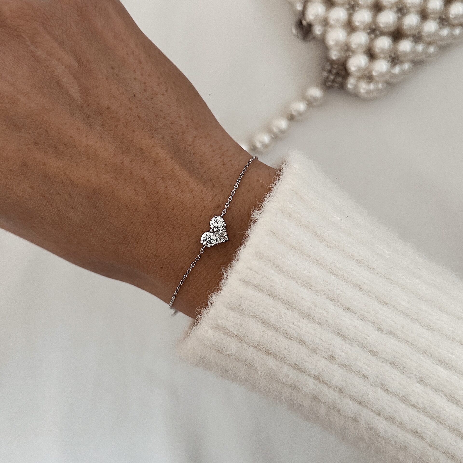 צמיד לב כסף אמיתי 925 משובץ זרקונים נוצצים על פרק יד של אישה עם סוודר לבן