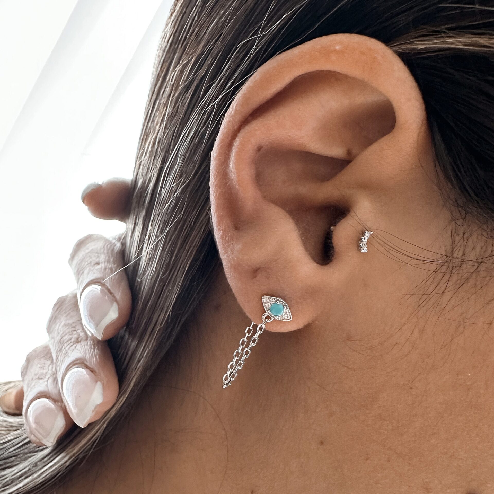 עגיל כסף 925 עם תליון בצורת עין משובץ טורקיז וזירקונים, עם שרשראות כפולות, על אוזן של אישה