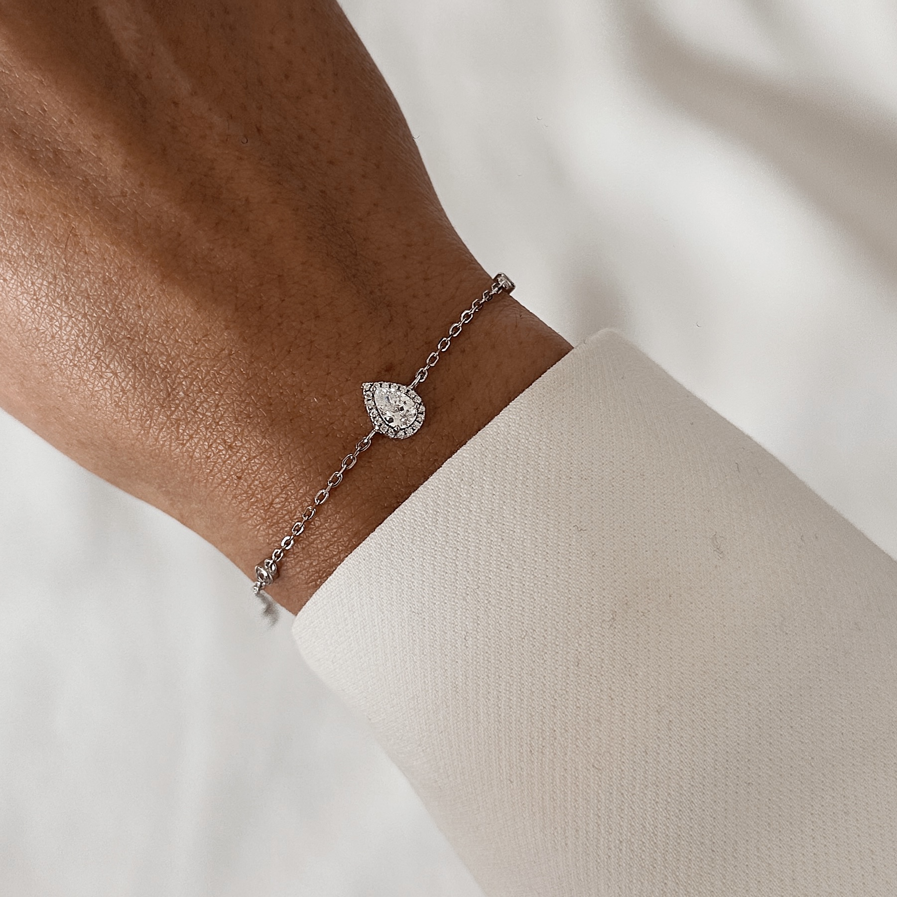 צמיד טיפה כסף אמיתי 925 משובץ זרקונים נוצצים על פרק יד של אישה עם חולצה לבנה