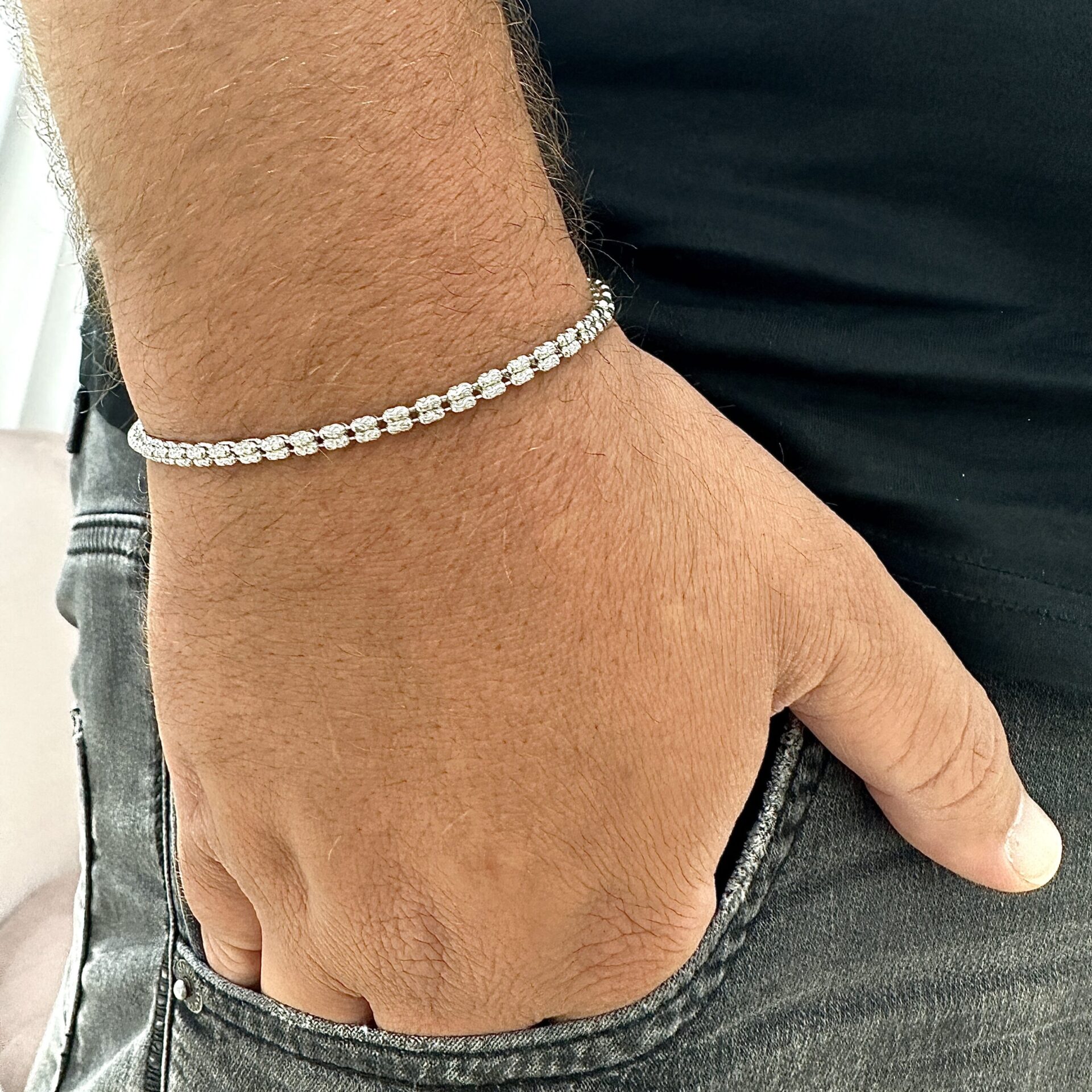 צמיד טניס כסף אמיתי 925 משובץ זרקונים נוצצים על יד של גבר עם חולצה שחורה ומכנסי ג'ינס