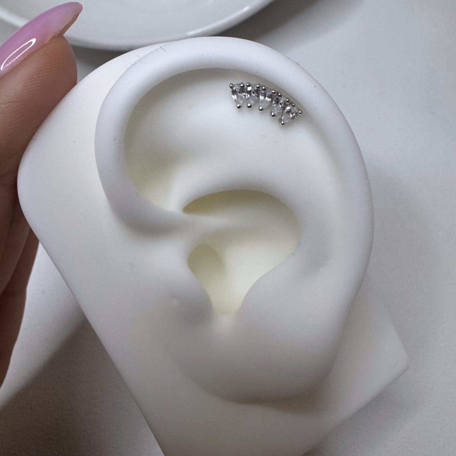 עגיל טיפות צמוד ורסנו הליקס בצורת שורת זרקונים מונח על דגם אוזן מסיליקון להצגת מראה העגיל באוזן. כסף אמיתי 925