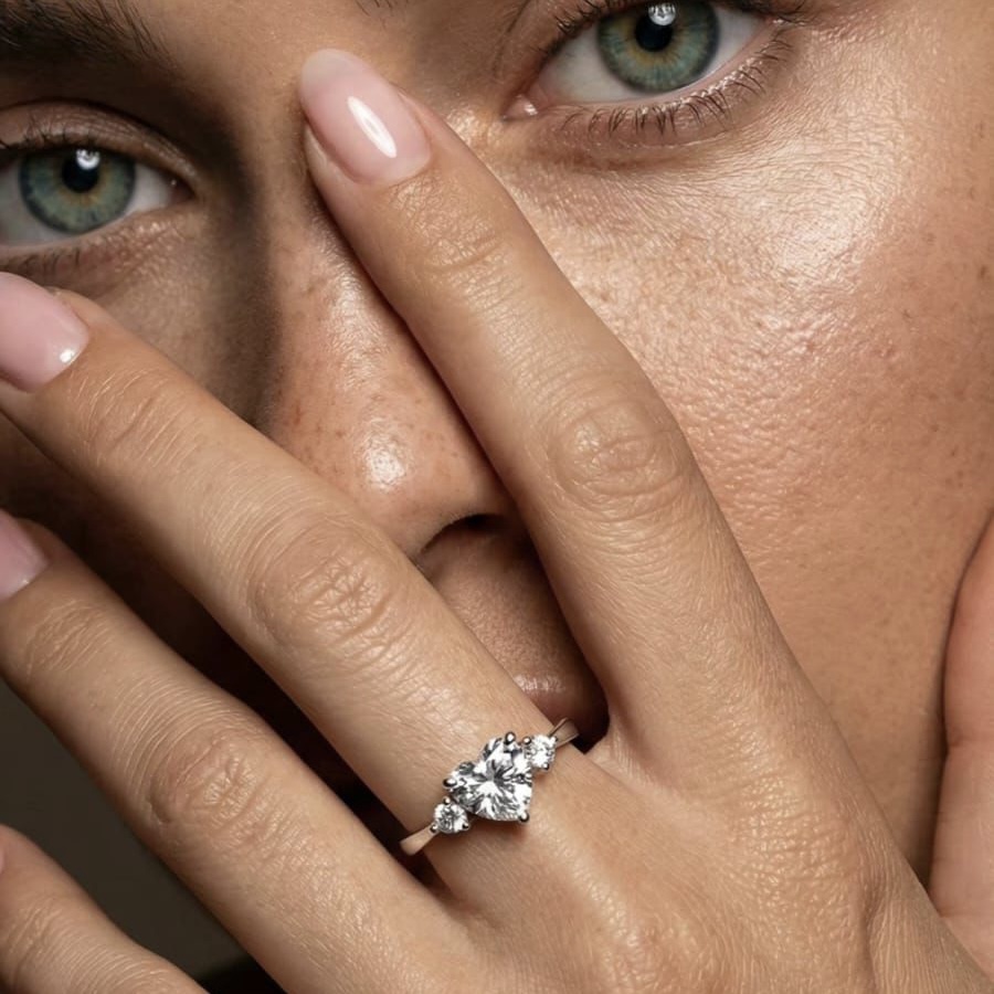 טבעת כסף 925 עם אבן מרכזית בצורת לב ושני זרקונים קטנים על אצבע של אישה, קלוז־אפ המציג את הברק והעיצוב האלגנטי.